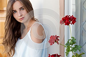 Portrait of a beautiful cute girl with blue eyes and dark curly hair in the courtyard near the wall with the window and flowers