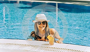 Portrait of beautiful cute smiling young woman lady girl in a bikini, hat, and sunglasses holding tropical lemonade