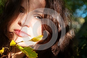 Portrait of a beautiful dark-haired young sexy seductive enigmatic woman in the forest in sunlight with green leaves