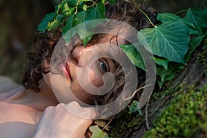 Portrait of a beautiful dark-haired young woman in ivy-crowned old willow tree with fine naked shoulders and deep peace