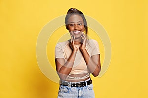 Portrait of beautiful, delightful, young african girl in casual clothes posing with tender smile against yellow studio