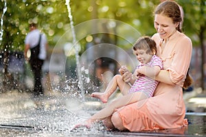 Portrait of beautiful disabled girl in the arms of his mother having fun in fountain of public park at sunny summer day. Child