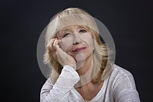 Portrait of a beautiful elderly woman. A smiling blonde sits with her hand resting her cheek. Happy maturity. Close-up. Black