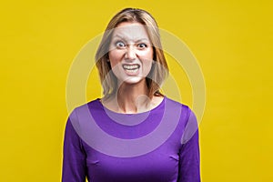 Portrait of beautiful emotional woman with clenched teeth pretending to be aggressive. indoor studio shot isolated on yellow