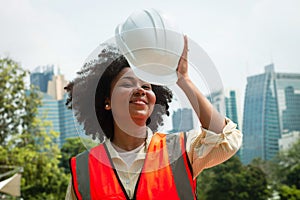 Portrait of a beautiful engineer African American woman Wearing a white hat, orange shirt, city background