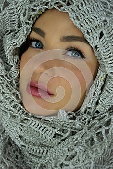 Portrait of a beautiful European blue eyed girl`s face wrapped by big soft knitted gray scarf. Winter stock image
