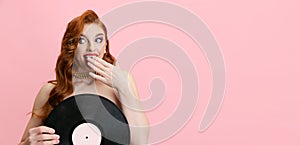 Portrait of beautiful excited Caucasian woman, singer holding vinyl record isolated over pink background. Flyer