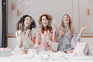 Portrait of beautiful excited women 20s wearing dresses celebrating bridal shower in posh apartment, with champagne and falling c