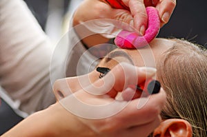 Portrait of beautiful face of young woman getting make-up. The artist is applying eye mascara on her eyes. The lady