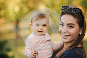 Portrait of beautiful family in the park. Mom and daughter togehter in autumn. Beautiful ten month baby on mother`s