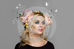 Portrait of a beautiful fashion model with red lips and blue eyes with coronet from flowers in curly blonde hair