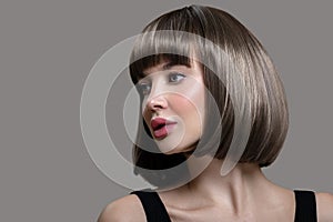 Portrait of beautiful fashion woman with bob hairstyle. Thick short wig. Gray background