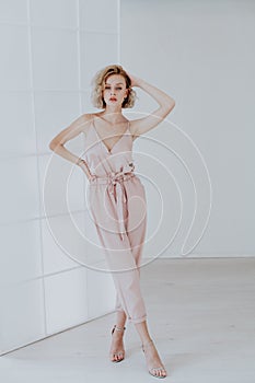 Portrait of a beautiful fashionable blonde woman in a pink jumpsuit on a white background
