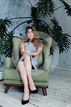 Portrait of a beautiful fashionable woman in a gray dress sitting in a green chair