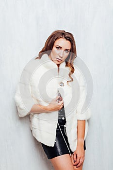 Portrait of a beautiful fashionable woman with hair curls in a white fur coat