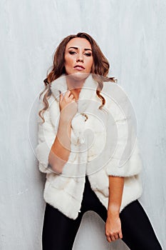 Portrait of a beautiful fashionable woman with hair curls in a white fur coat