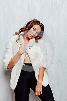 Portrait of a beautiful fashionable woman with hair curls in a white fur coat