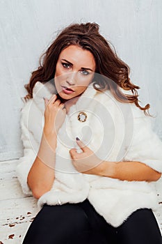 Portrait of a beautiful fashionable woman with hair curls in a white fur coat