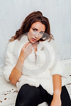 Portrait of a beautiful fashionable woman with hair curls in a white fur coat
