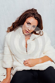 Portrait of a beautiful fashionable woman with hair curls in a white fur coat