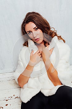 Portrait of a beautiful fashionable woman with hair curls in a white fur coat