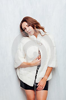 Portrait of a beautiful fashionable woman with hair curls in a white fur coat