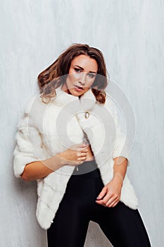 Portrait of a beautiful fashionable woman with hair curls in a white fur coat in winter