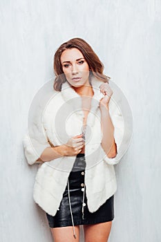 Portrait of a beautiful fashionable woman with hair curls in a white fur coat in winter