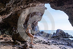 Portrait of beautiful fashionable woman in white bikini posing at the rock beach. Young Asian woman dressed in swimsuit standing