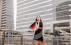 Portrait of beautiful female in black dress smling and holding shopping bags in city