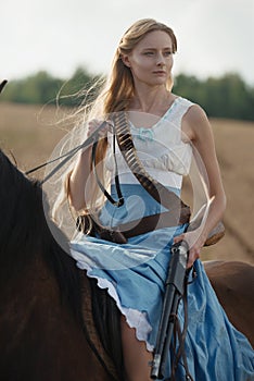 Portrait of a beautiful female cowgirl with shotgun from wild west riding a horse in the outback.