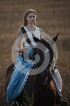 Portrait of a beautiful female cowgirl with shotgun from wild west riding a horse in the outback.