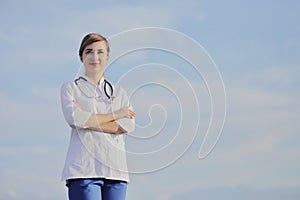 Portrait of a beautiful female doctor or nurse against blue sky with clouds