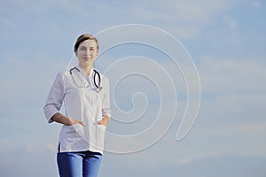 Portrait of a beautiful female doctor or nurse against blue sky with clouds
