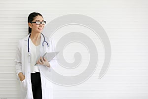 Portrait of beautiful female doctor wearing eye glasses standing and holding tablet computer in front of white background