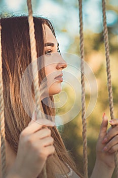 Portrait of beautiful female face near ropes of swing, girl swinging on nature, young woman relaxes, leisure activity, lifestyle