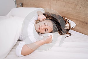 Young woman sleeping in bed. Portrait of beautiful female resting on comfortable bed with pillows In white bedding In light