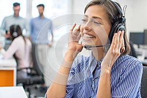 Portrait of beautiful friendly female customer services agent with headset working in call center.