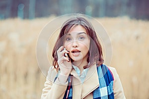 Portrait of a beautiful frustrated woman talking on the mobile phone in a park with a light brown unfocused park nature background