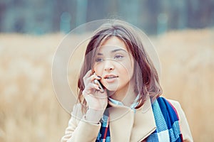 Portrait of a beautiful frustrated woman talking on the mobile phone in a park with a light brown unfocused park nature background