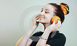 Portrait of beautiful funny girl with orange halves like headphones for listening to music, woman fooling around, concept music of