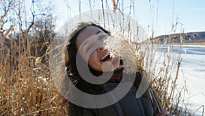 Portrait of a beautiful girl on the bank of a frozen river enjoying nature, laughing and playing with yellow cane