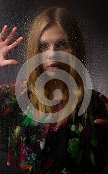 Portrait of a beautiful girl behind wet glass