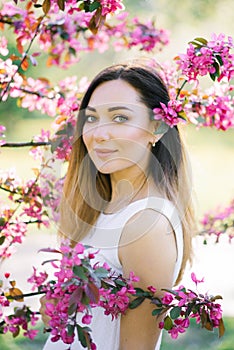 Portrait of a beautiful girl with big eyes in a white dress and blooming pink Apple blossoms