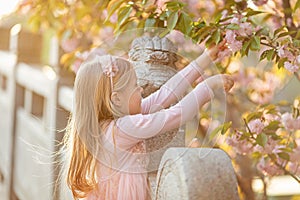 Portrait of beautiful girl with blooming flowers. Cherry blossom. Little caucasian girl with long blonde hair standing in the park