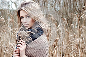 Portrait of a beautiful girl with blue eyes in a grey jacket in the field among trees and tall dry grass, tinted in shades of gray