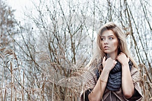 Portrait of a beautiful girl with blue eyes in a grey jacket in the field among trees and tall dry grass, tinted in shades of gray photo