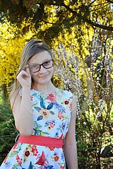 Portrait of beautiful girl with brown hair looking over glasses and surprised. Young smiling teneeger in green spring park resting