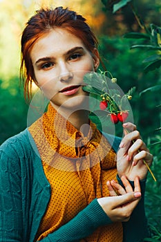 portrait of a beautiful girl with brown hair who holds a twig with wild strawberries. harvesting