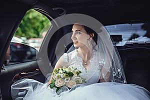 Portrait of a beautiful girl in the car. The bride holds a wedding bouquet in her hands and looks at the street through the car